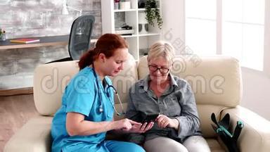 养老院的护士坐在沙发上帮助老年妇女使用智能手机